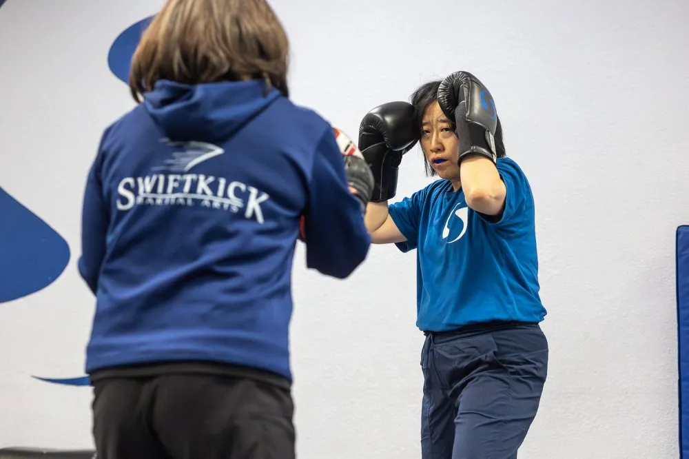 Woman practicing boxing drills with instructor at a martial arts class