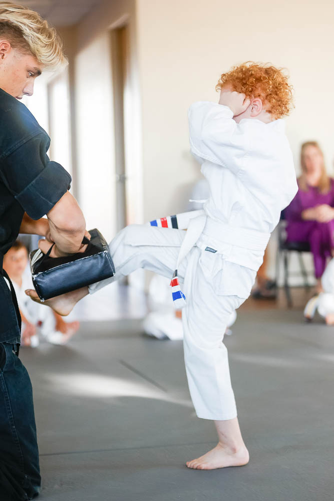 Young swiftkick student kicking a pad an instructor is holding