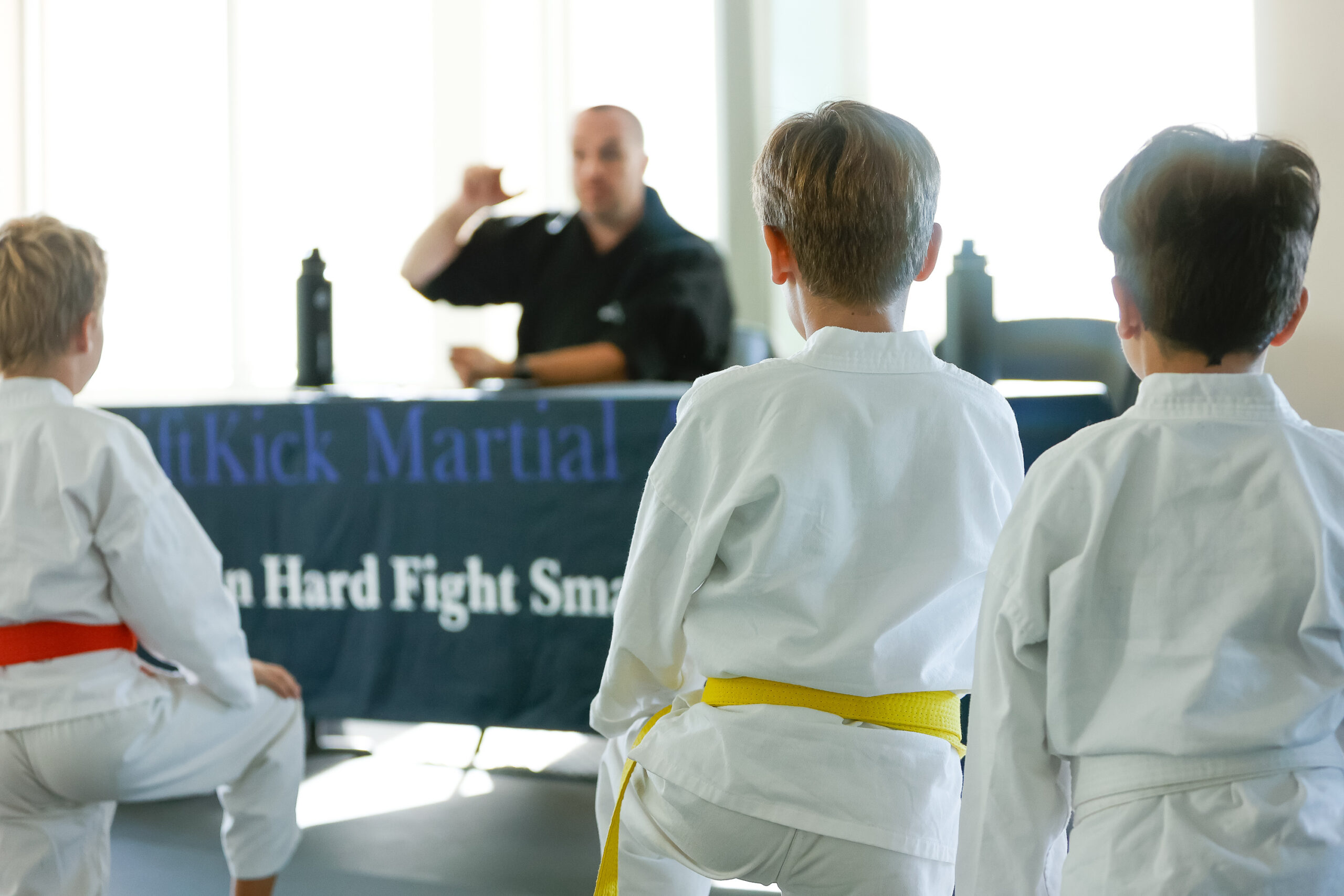 A group of young orange and yellow belt students listening to martial art instructor.