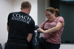 Woman knee striking a pad while an instructor holds it.