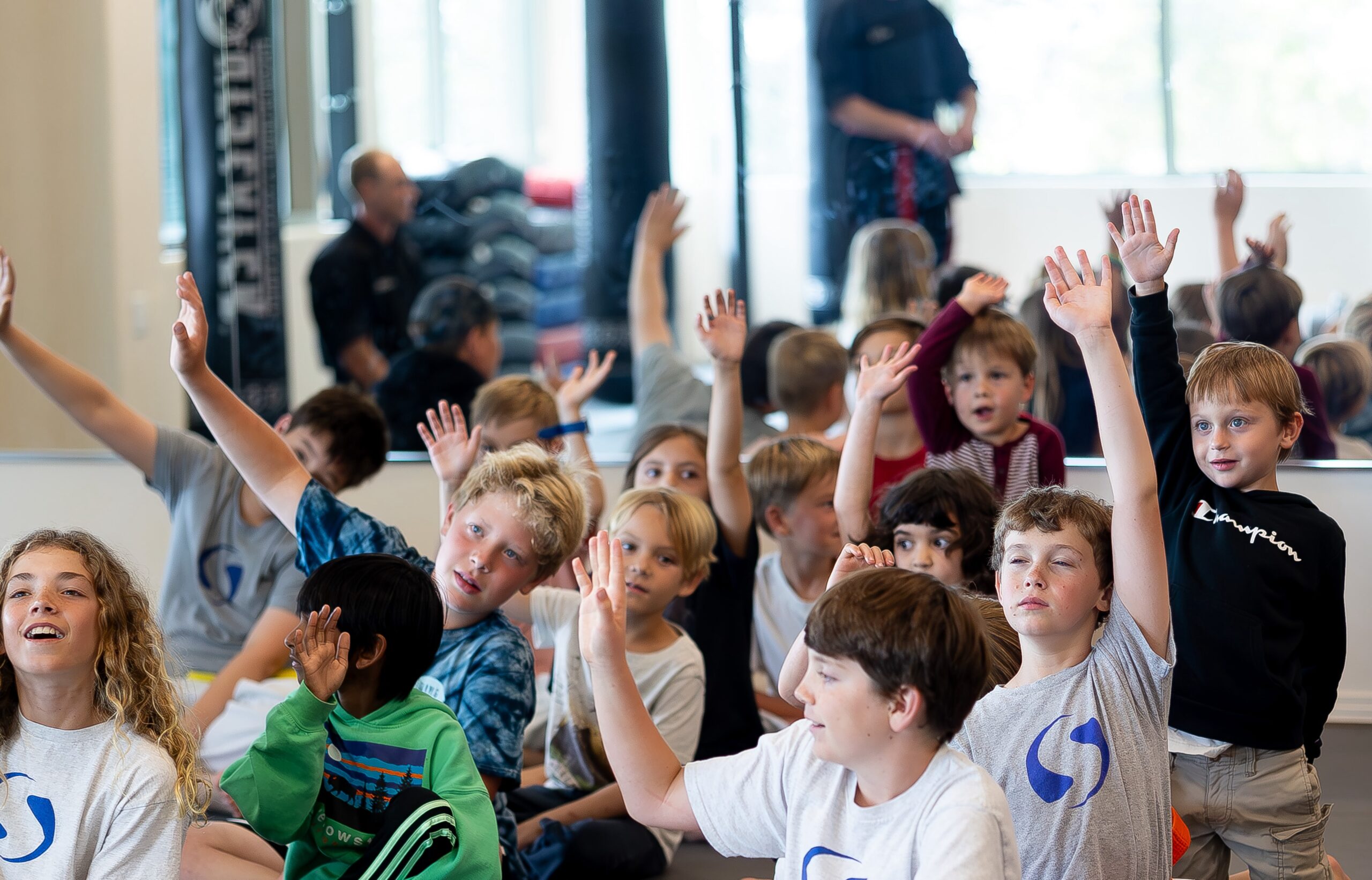 swiftkick-summer-camp a group of well behaved kids raising their hands politely.