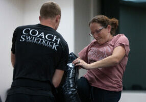 Woman knee striking a pad while an instructor holds it.